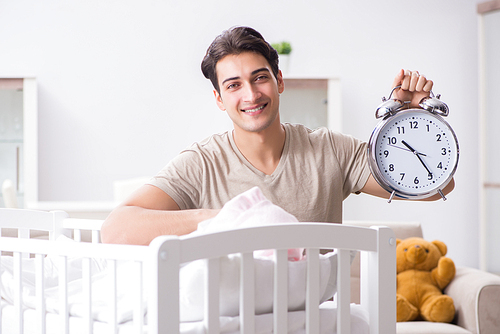 Young dad with clock near newborn baby bed cot