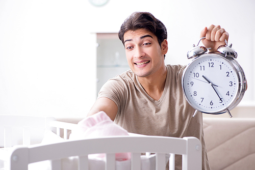Young dad with clock near newborn baby bed cot