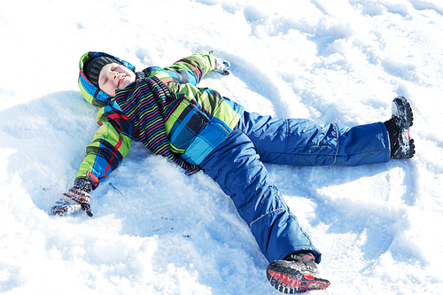 Happy kid lies on snow in winter park