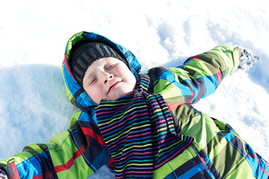 Happy kid lies on snow in winter park