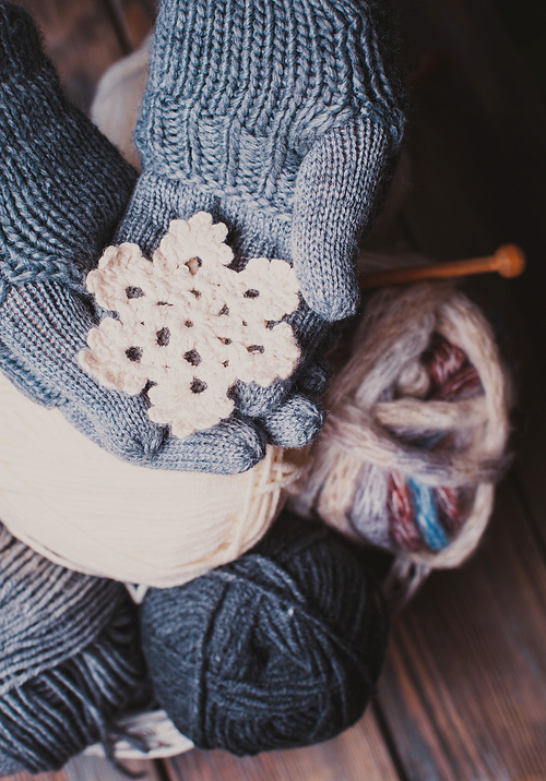 Hands in a grey gloves holding white knitted snowflake as a winter symbol