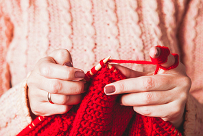 The hands that hold needles and knitting a red warm jacket
