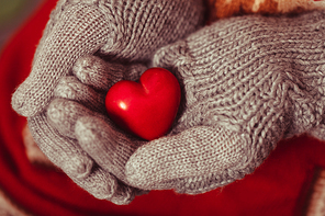 Close-up of hands in grey knitted mittens holding red heart