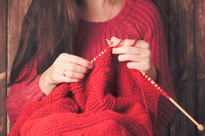 Woman holds needles and knitting a red warm jacket