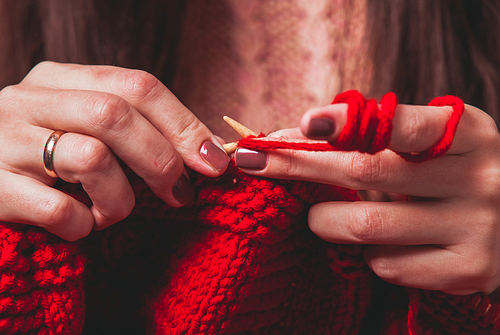 The hands that hold needles and knitting a red warm jacket