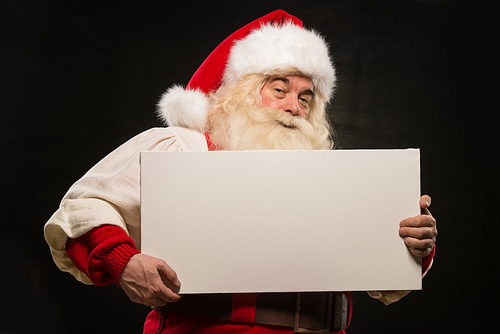 Santa Claus holding white blank sign with fun and smile standing against dark background