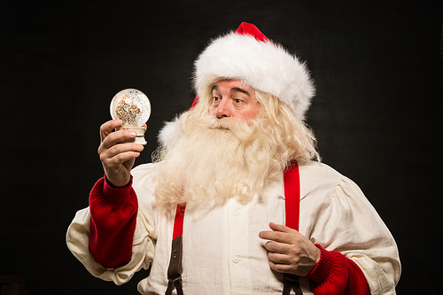 Santa Claus holding snow globe against dark background