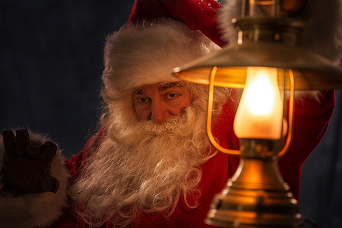 Santa Clause walking outdoors under falling snow with vintage lamp
