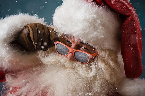 Santa Claus wearing sunglasses dancing outdoors at North Pole in snowfall. He is celebrating Christmas after hard work
