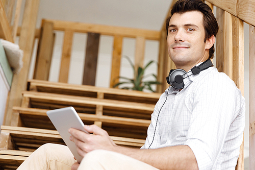 Portrait of young businessman sitting at the stairs in office with headphones
