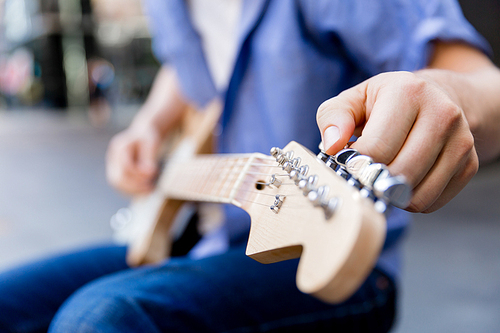 Hands of musician tuning his guitar outside
