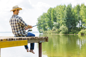 Young guy in hat sitting on bridge and fishing
