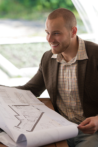 Happy businessman working with blueprint at sidewalk cafe