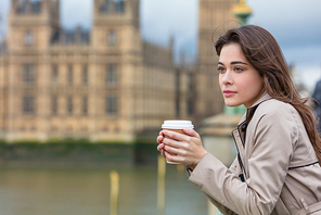 Beautiful sad, depressed or thoughtful young woman in London on Westminster Bridge over the River Thames drinking takeout coffee by Big Ben