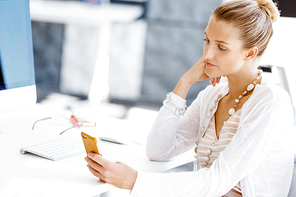 Attractive woman sitting at desk in office holding mobile phone