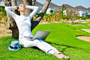 Young girl dressed in white rest lying on a tree with her laptop.