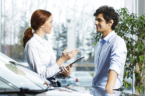 Young woman dealer in auto salon presenting car to customer