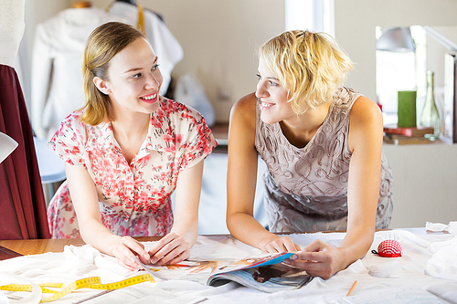 Two attractive women at dressmakers choosing design