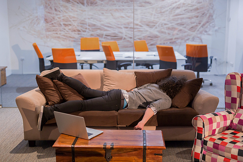 A young casual businessman sleeping on a sofa during a work break in a creative office