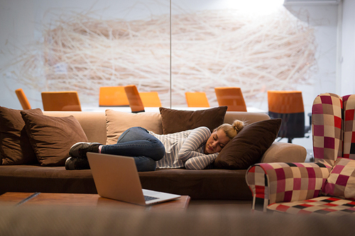 A young casual business woman sleeping on a sofa during a work break in a creative office