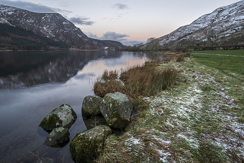 Beautiful sunrise landscape image in Winter of Llyn Cwellyn in Snowdonia National Park with snow capped mountains in background