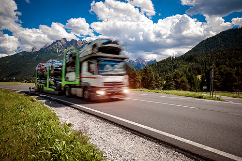 Truck trailer transports new cars rides on highway, Italy natural landscape Alps. Warning - authentic shooting there is a motion blur.