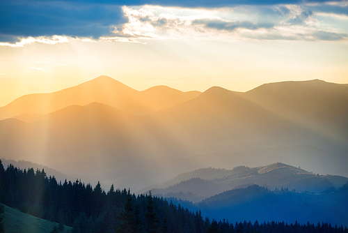 Beautiful sunset in the mountains. Landscape with sun shining through orange clouds