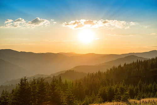 Sunset in the mountains with forest and big shining sun on dramatic sky