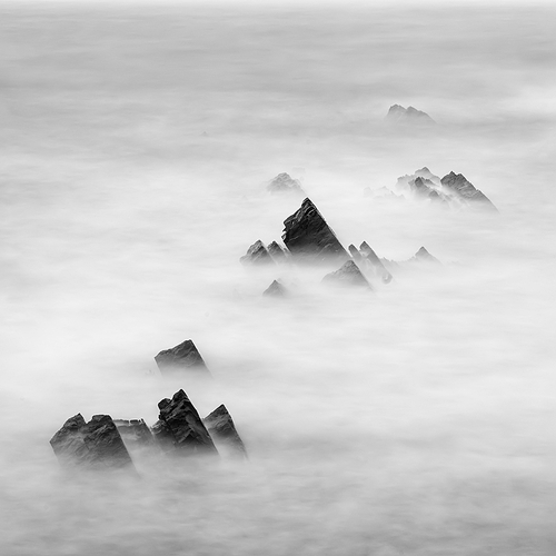 Stunning long exposure landscape image of sea over rocks during sunset in black and white