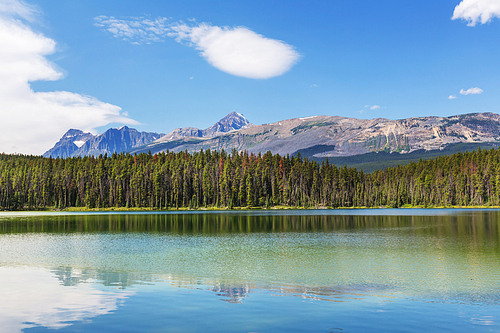 Serene scene by the mountain lake in Canada with reflection of the rocks in the calm water.