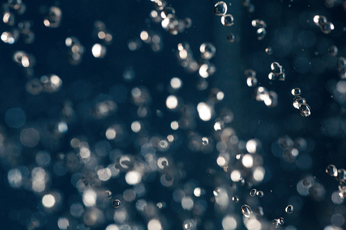 Defocused drops of water fly over deep blue background, rain or shower