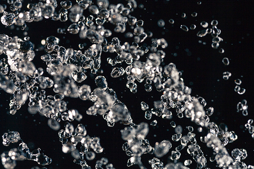 Small rain drops levitate on black background, freezed in air