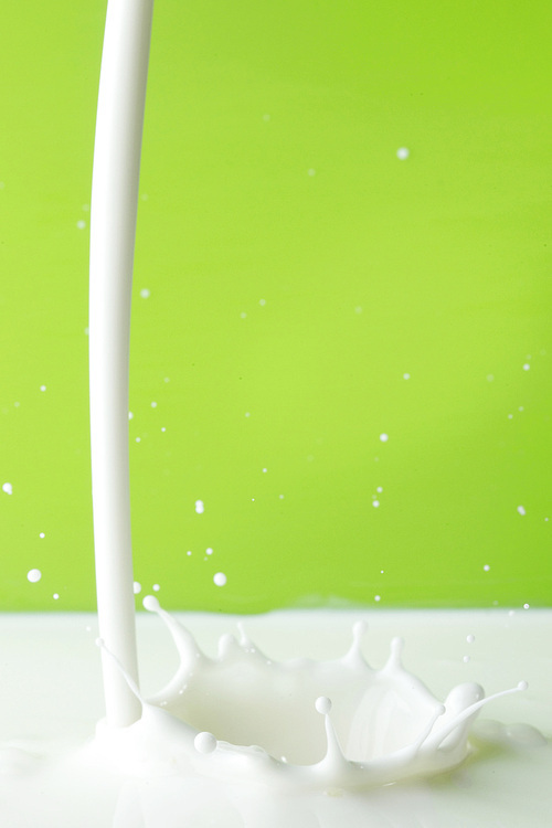 Pouring milk splash on green background close-up