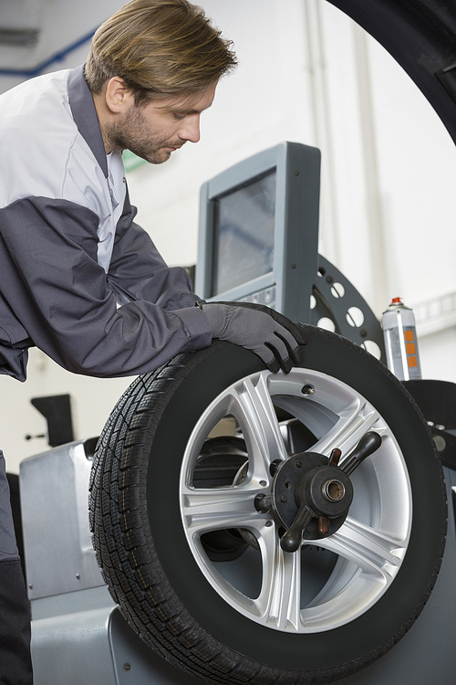 Cropped image of automobile mechanic repairing car's wheel in workshop