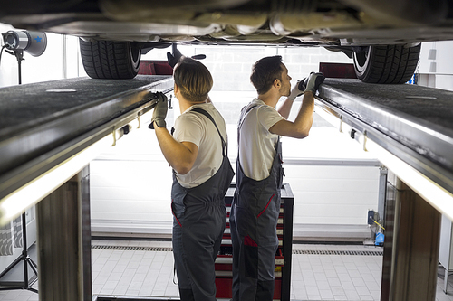 Side view of maintenance engineers examining car in repair shop