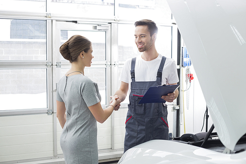 Smiling maintenance engineer shaking hands with female customer in car repair shop