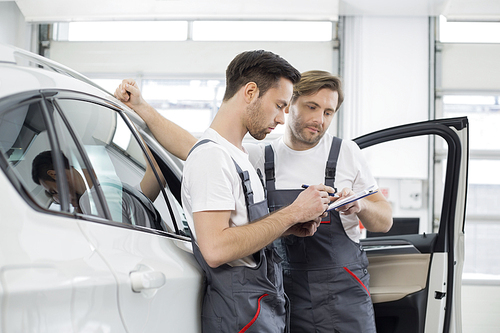 Automobile mechanics checking checklist while standing by car in workshop