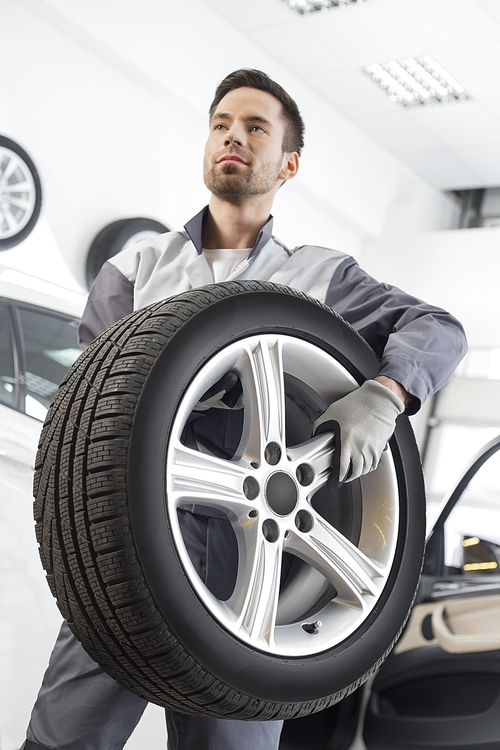 Young maintenance engineer carrying tire in automobile store