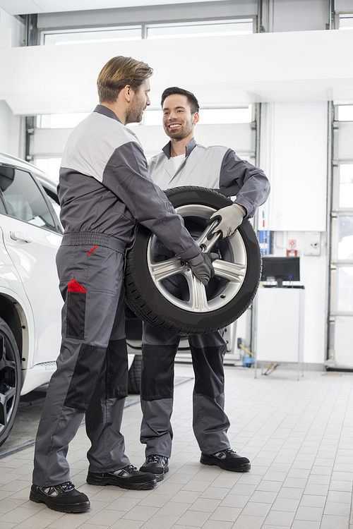 Full-length of maintenance engineers carrying tire in car workshop