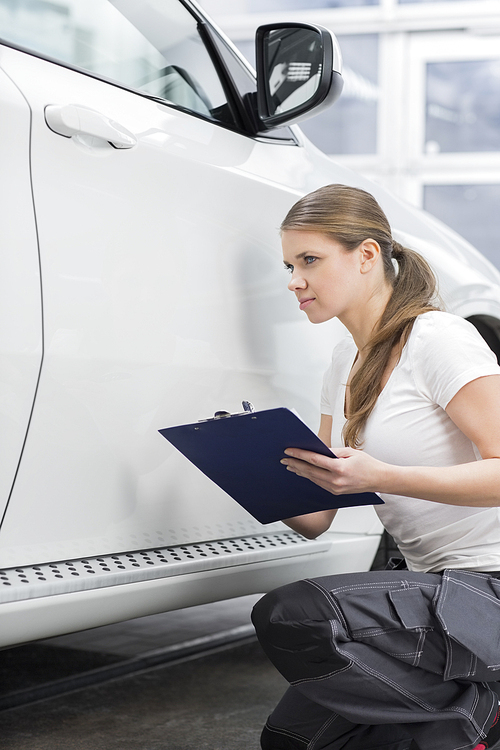 Female mechanic holding clipboard while examining car body at repair shop