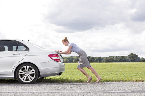 Full length side view of businesswoman pushing broken down car at countryside