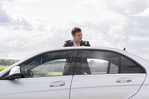 Young businessman leaning on broken down car at countryside