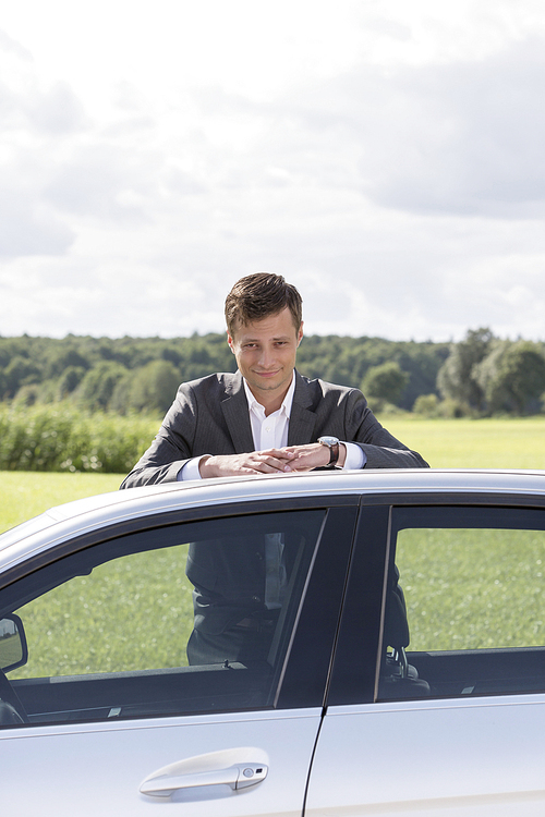Portrait of young businessman leaning on broken down car at countryside