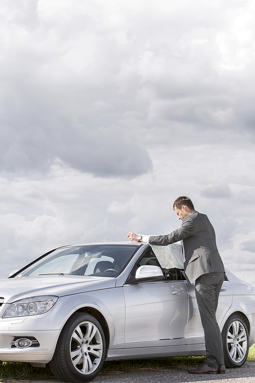 Full length side view of businessman reading map by car at countryside