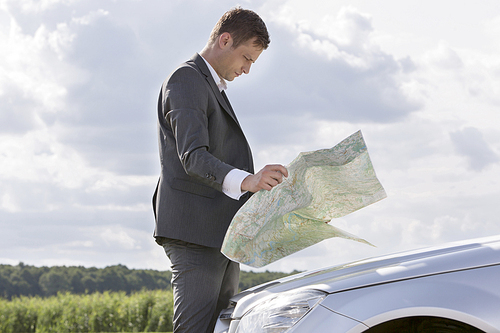 Side view of young businessman reading map by car at countryside