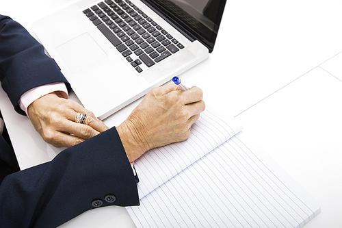 Cropped image of businesswoman with laptop writing in notebook on office desk