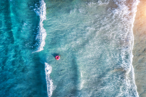 aerial view of a young woman swimming with the donut swim ring in the clear blue sea with beautiful waves at  in summer. tropical aerial landscape with girl, azure water. top view. travel