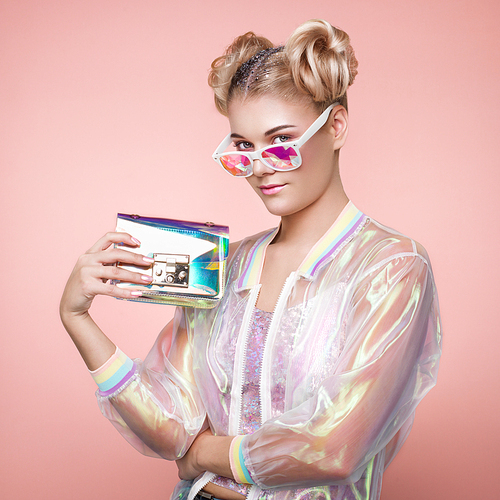 Blonde Young Woman in Holographic Jacket. Lady in Stylish Pink Eyeglasses. Model with Holographic Foil Handbags. Beauty Fashion Make-up