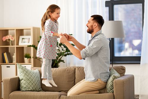 family, childhood and fatherhood concept - happy father and little daughter jumping on sofa and having fun at home