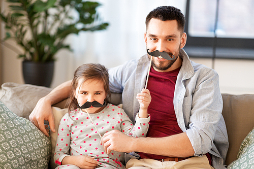 family, childhood and fatherhood concept - happy father and little daughter with mustaches party props having fun at home